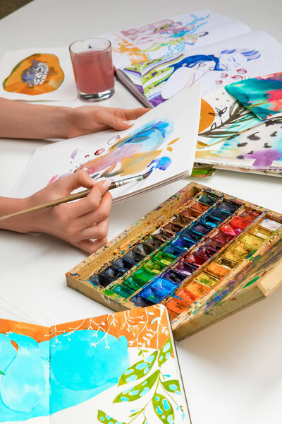 selective focus of female hands painting with watercolors paints and paintbrush on white album