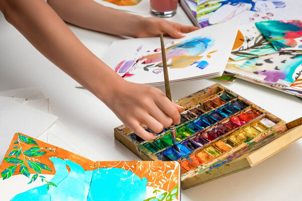 selective focus of female hands mixing watercolor paints in palette and hold paper with picture