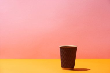 Kağıt kahve Kupası sarı yüzey ve pembe arka plan üzerinde