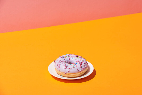 вкусный пончик с блюдцем на желтой поверхности и розовый фон
