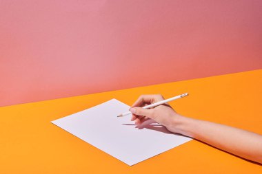 cropped view of woman writing on paper on yellow desk and pink background clipart