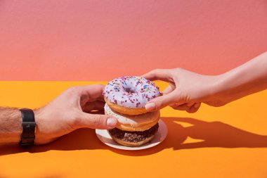 kadın ve adam sarı resepsiyon ve pembe bir arka plan üzerinde uçan daire lezzetli donuts alarak görünümünü kırpılmış
