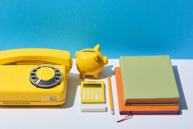 çok renkli defter, hesap makinesi, telefon ve kumbara beyaz resepsiyon ve mavi arka plan