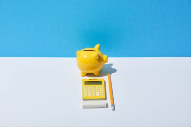calculator, piggy bank, eraser and pencil on white desk and blue background clipart