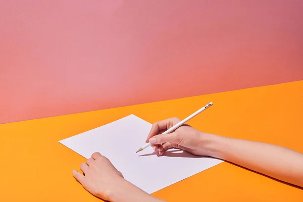 cropped view of woman writing on paper sheet by pencil on yellow desk