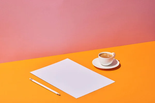 paper sheet, pencil and coffee cup on yellow desk and pink background