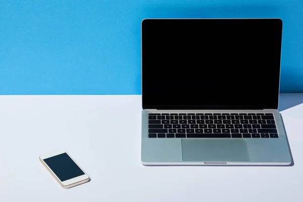 笔记本电脑与空白屏幕和智能手机在白色的办公桌和蓝色的背景 — 图库照片