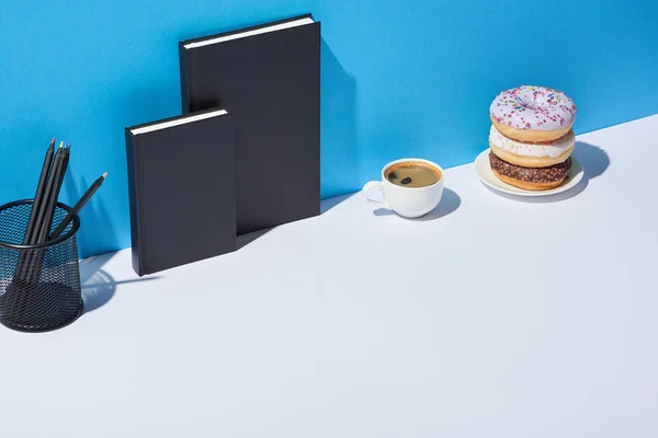 美味的甜甜圈 咖啡杯 铅笔架和笔记本上的白色办公桌和蓝色背景 — 图库照片