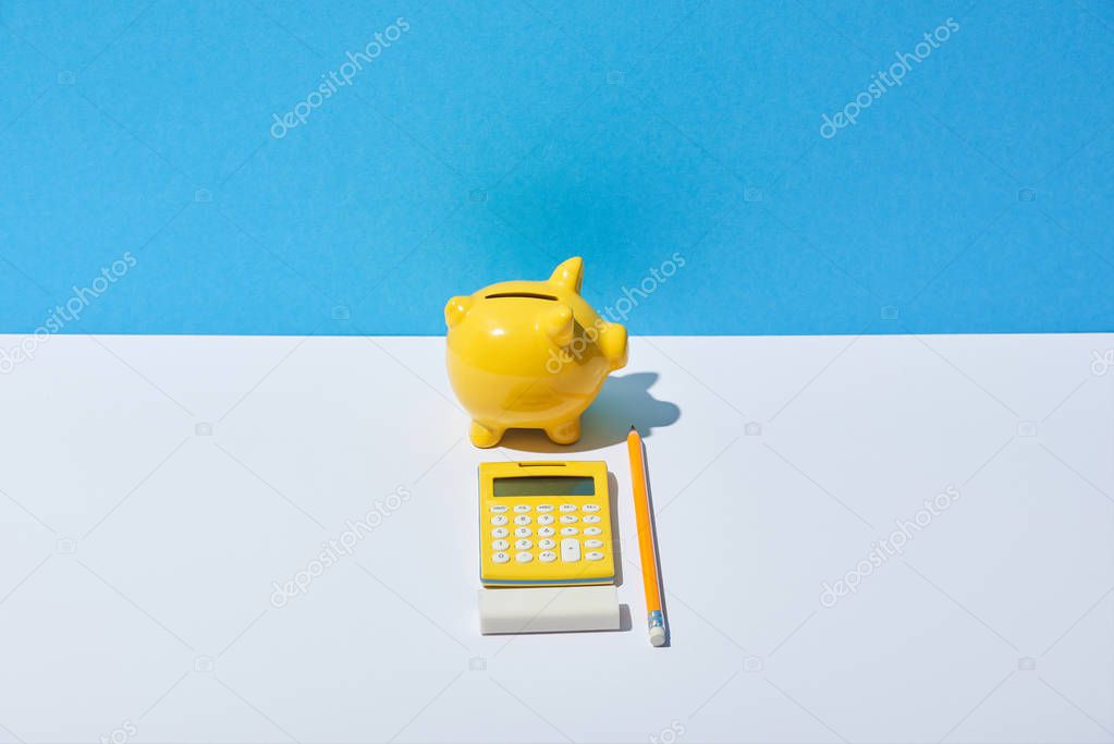 calculator, piggy bank, eraser and pencil on white desk and blue background