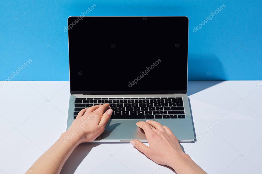 cropped view women using laptop with blank screen on white desk and blue background