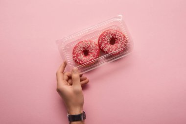 kutu donut elinde pembe bir arka plan üzerinde tutan adamın kırpılmış görünümü 