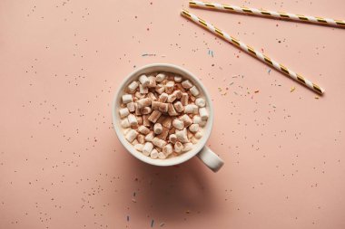 top view of sweet cacao with marshmallows near candy canes on pink background 