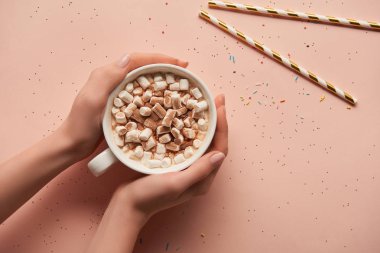 cropped view of woman holding cup of cocoa in hands on pink background 