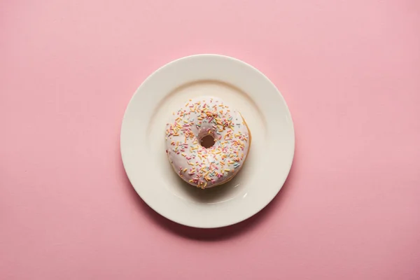 ピンクの背景に白い皿の上においしいドーナツのトップビュー — ストック写真