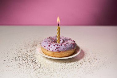 pembe arka plan üzerinde beyaz masada Parıltılar ile sırlı çörek ortasında yanan mum