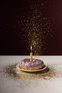 burning candle in middle of doughnut with falling sparkles on white table isolated on black clipart