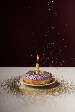 burning candle in middle of sweet doughnut with falling sparkles isolated on black clipart
