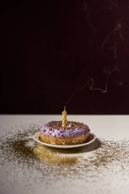 candle in middle of tasty doughnut with shiny sparkles on white table isolated on black