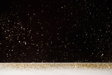 selective focus of golden sparkles falling on white table isolated on black  clipart