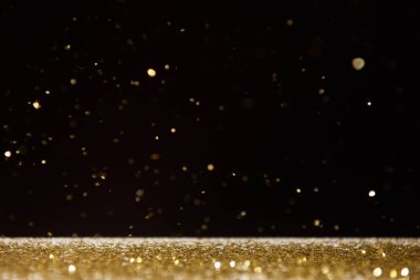 selective focus of golden sparkles falling on table isolated on black  clipart