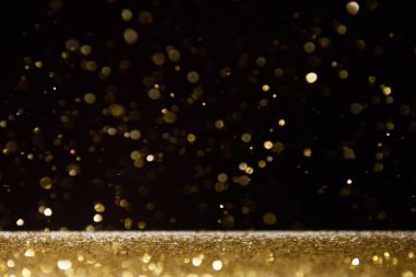 selective focus of golden shiny sparkles falling on table isolated on black  clipart