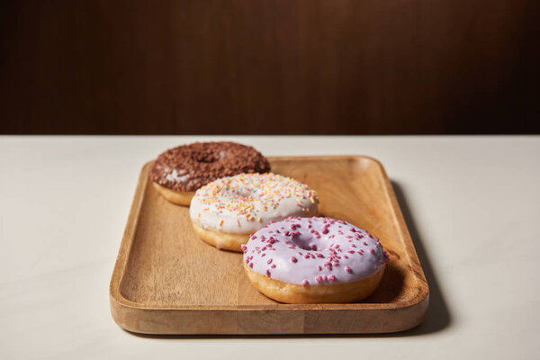 sweet glazed doughnuts with sprinkles on wooden cutting board