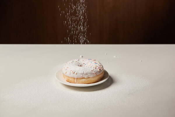 doughnut with icing and sprinkles with sifting sugar powder  on white table 