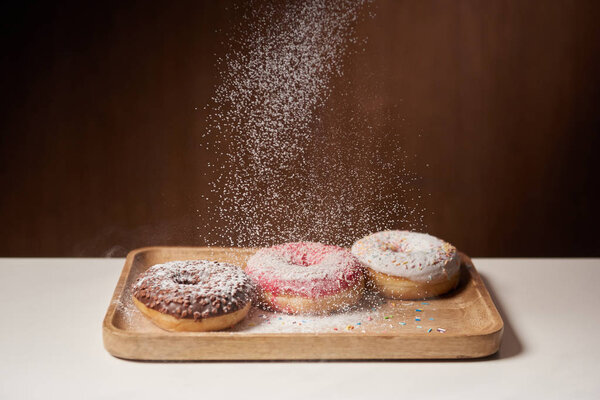 tasty donuts with sifting sugar powder on wooden cutting board
