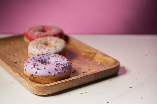 selective focus of sweet donut with icing and sprinkles on wooden cutting board 