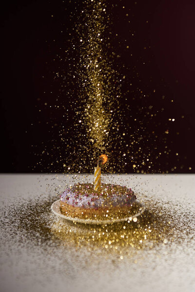 burning candle in middle of doughnut with falling golden sparkles isolated on black