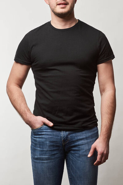 partial view of man with hand in pocket in denim and black t-shirt with copy space isolated on grey 