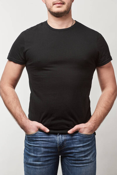 partial view of man with hands in pockets in black t-shirt with copy space isolated on grey 