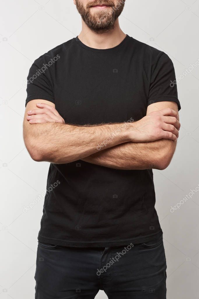 cropped view of bearded man with arms crossed in black t-shirt with copy space isolated on grey 