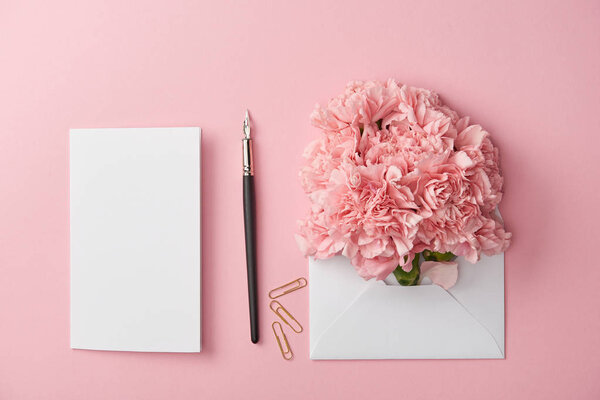 top view of blank card, ink pen and pink flowers in white envelope isolated on pink