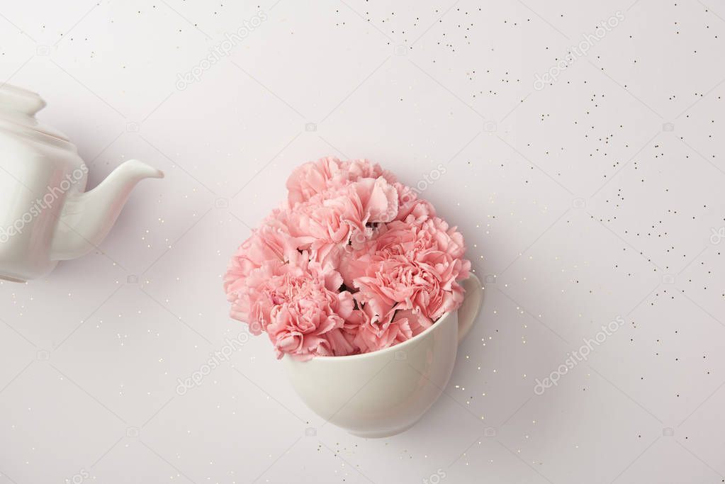 pink carnation flowers in cup and white kettle isolated on grey