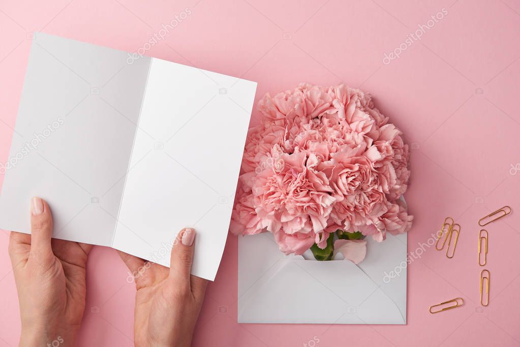 cropped shot of woman holding blank card and pink flowers in envelope isolated on pink