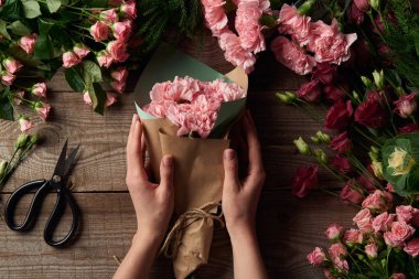 cropped shot of female hands holding beautiful bouquet and tender flowers with scissors on wooden surface 
