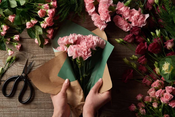 裁剪拍摄的妇女包裹美丽的花朵在工艺纸在木表面 — 图库照片