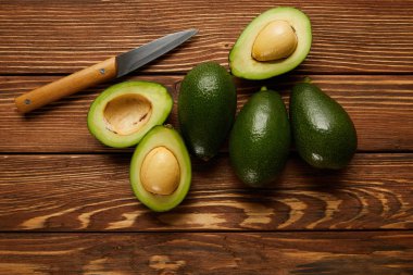 top view of avocados and knife on wooden background clipart