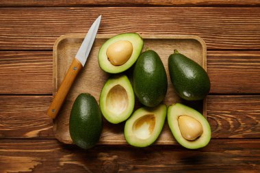 top view of avocados and knife on wooden background clipart