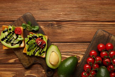 top view of toasts with avocados, cherry tomatoes on wooden background clipart
