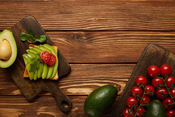 top view of toast with avocado and cherry tomatoes on wooden background