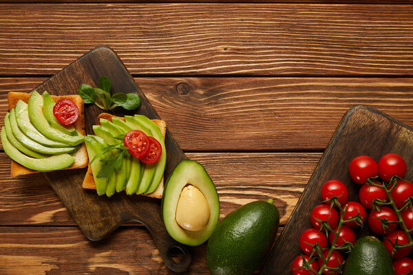 top view of toasts with avocados, cherry tomatoes on wooden background