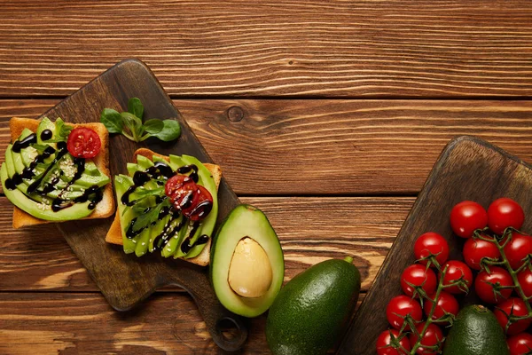 top view of toasts with avocados, cherry tomatoes on wooden background