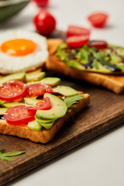kesme tahtası tost, çırpılmış yumurta, domates ve beyaz arka plan üzerinde avokado ile seçici odak