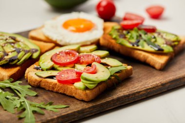 kesme tahtası tost, çırpılmış yumurta, domates ve beyaz arka plan üzerinde avokado ile seçici odak