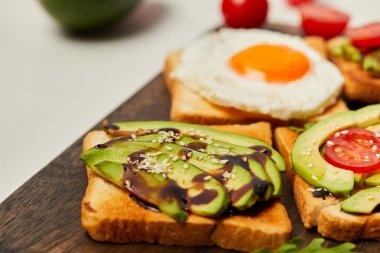 kesme tahtası tost, çırpılmış yumurta, domates ve beyaz arka plan üzerinde avokado ile seçici odak