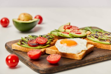 Ahşap kesme tahtası tost, çırpılmış yumurta, domates ve gri arka plan üzerinde avokado ile seçici odak