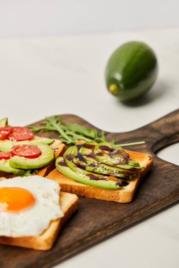 Ahşap kesme tahtası tost, çırpılmış yumurta, domates ve gri arka plan üzerinde avokado ile seçici odak