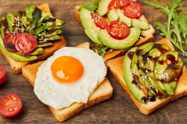 selective focus of toasts with scrambled egg, cherry tomatoes and avocado on wooden background clipart